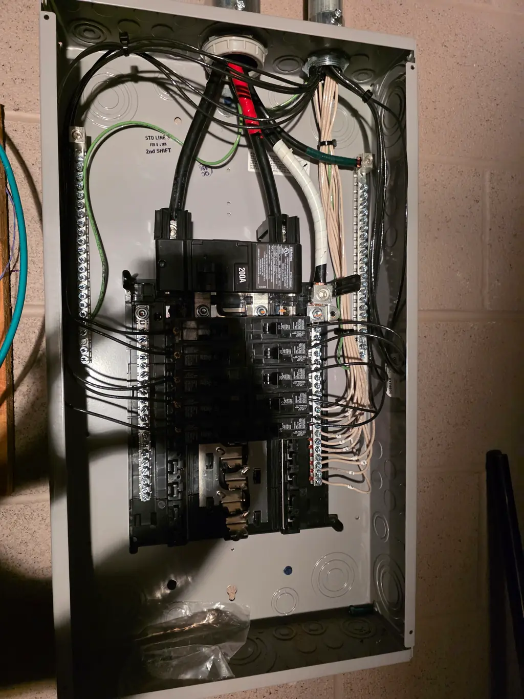 A finished 200 amp Siemens load centre with the door open, conductors dressed and breakers landed, mounted on a block wall.